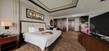 Ein Hotelzimmer mit einem großen Bett, einem Schreibtisch mit Fernseher und einem durchgehenden Türspalt einsehbaren Badezimmer.
