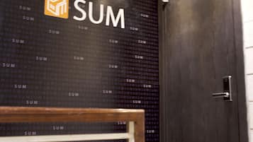 A modern interior with a dark wooden door, a wall with repeated 'SUM' branding, and a metal-framed shelf.