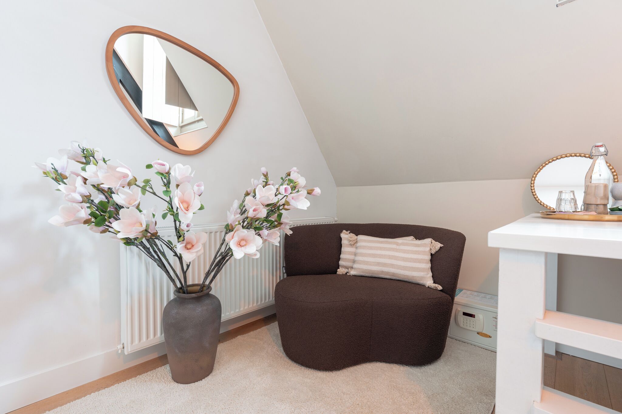A modern room with a brown sofa, a white console table, a mirror, and two vases with flowers.