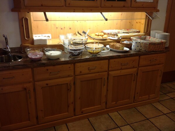 A kitchen with wooden cabinets, a sink, and various food items on the counter. - Hotel Belvedere (Panchia)