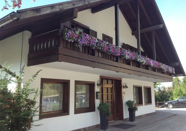 Un chalet traditionnel doté d’un balcon orné de fleurs, d’une porte en bois et de plantes en pot à l’entrée.