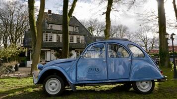 Une voiture bleue d’époque est garée devant un bâtiment portant l’inscription « Restaurant n° 15, Hoog Soeren ».