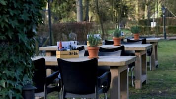 Des tables en bois installées à l’extérieur, accompagnées de chaises noires, de plantes en pot et d’une enseigne portant l’inscription « n° 15 ».