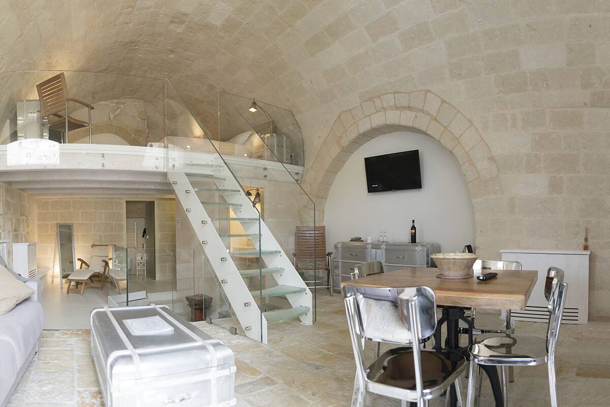 Un'ampia zona giorno con soffitto ad arco, una scala che conduce a un piano superiore, un'area pranzo con tavolo e sedie in legno e un televisore a schermo piatto montato a parete.