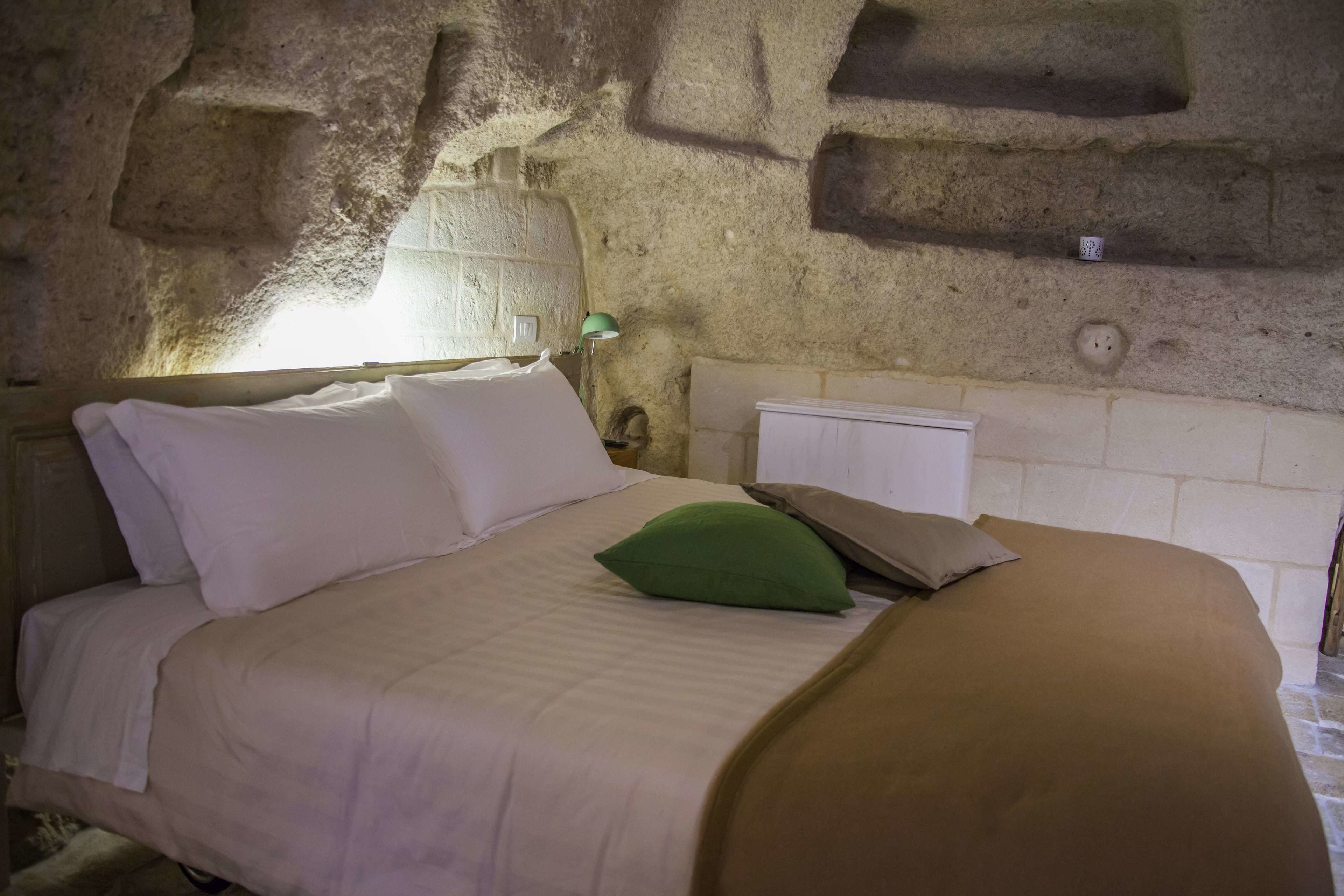 A bed with white and green pillows, a beige blanket, and a green pillow on a stone wall bed.