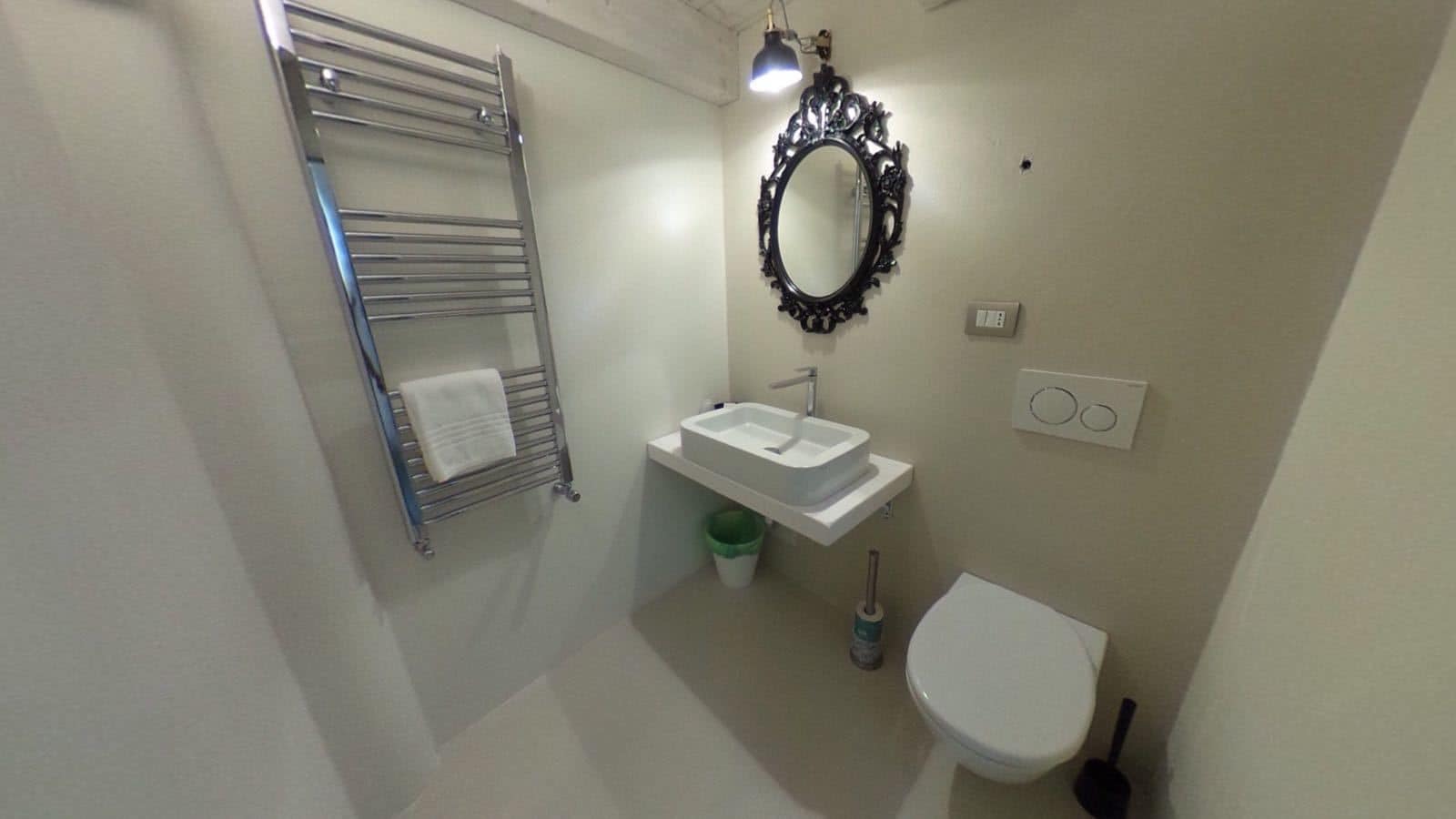 Une petite salle de bain équipée d’un porte-serviettes, d’un lavabo, d’un miroir, de toilettes et d’un luminaire.
