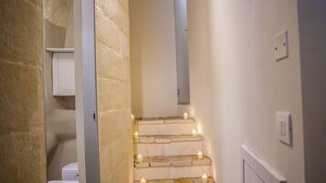 Una escalera con velas, un inodoro blanco y un muro de piedra.