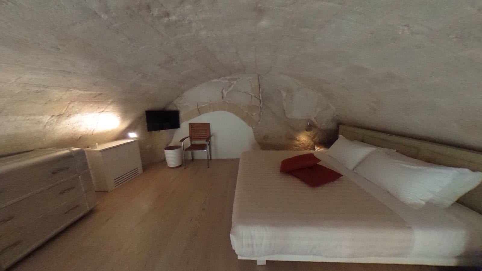 A cozy attic bedroom with a bed, a chair, a dresser, and a TV mounted on the wall.