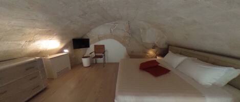 A cozy attic bedroom with a bed, a chair, a dresser, and a TV mounted on the wall.