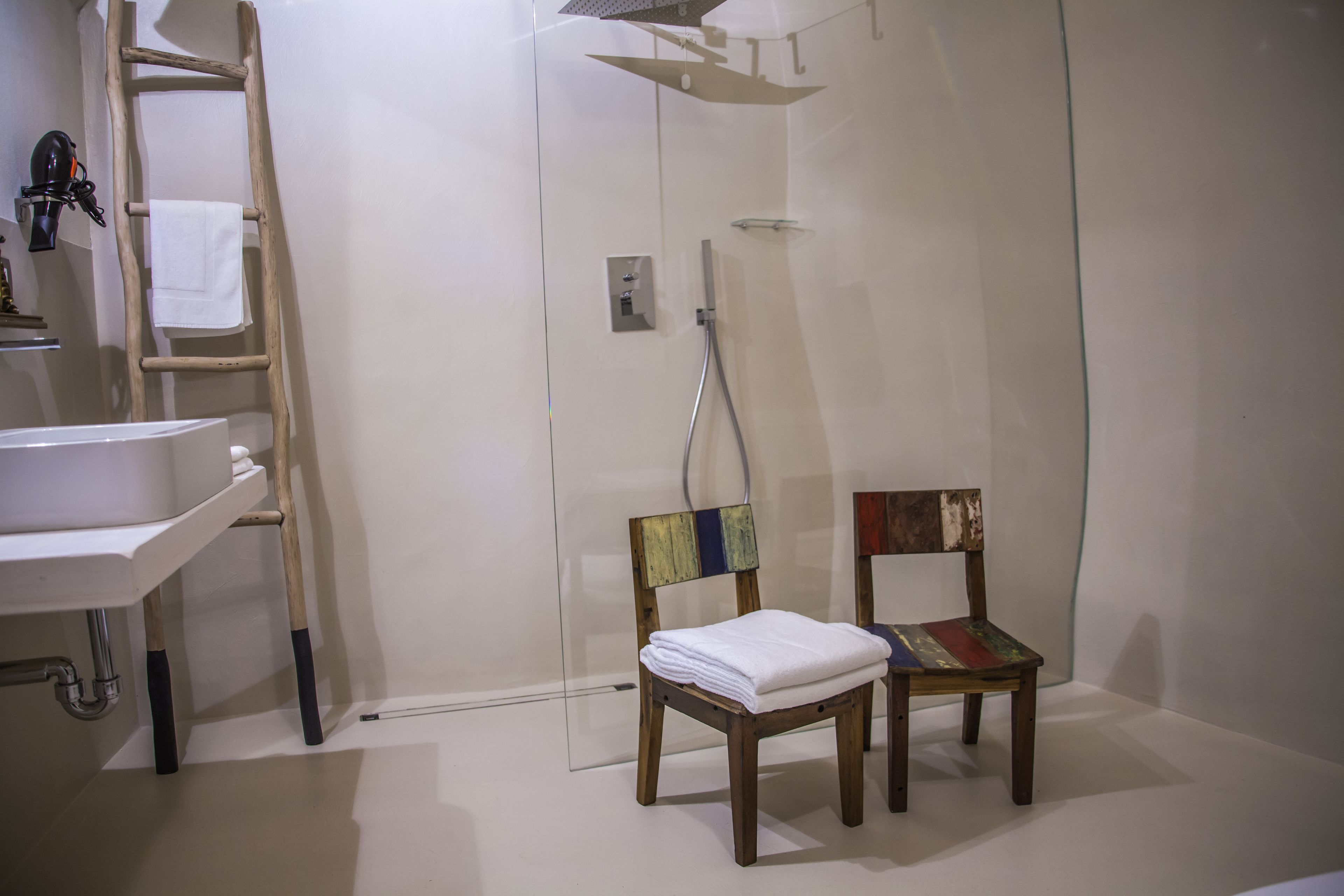 Un baño con un lavamanos blanco, una escalera de madera y una silla con respaldo colorido.