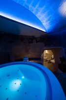 A spa area with a hot tub, stone walls, and a view into a bathroom with a bathtub and sink.