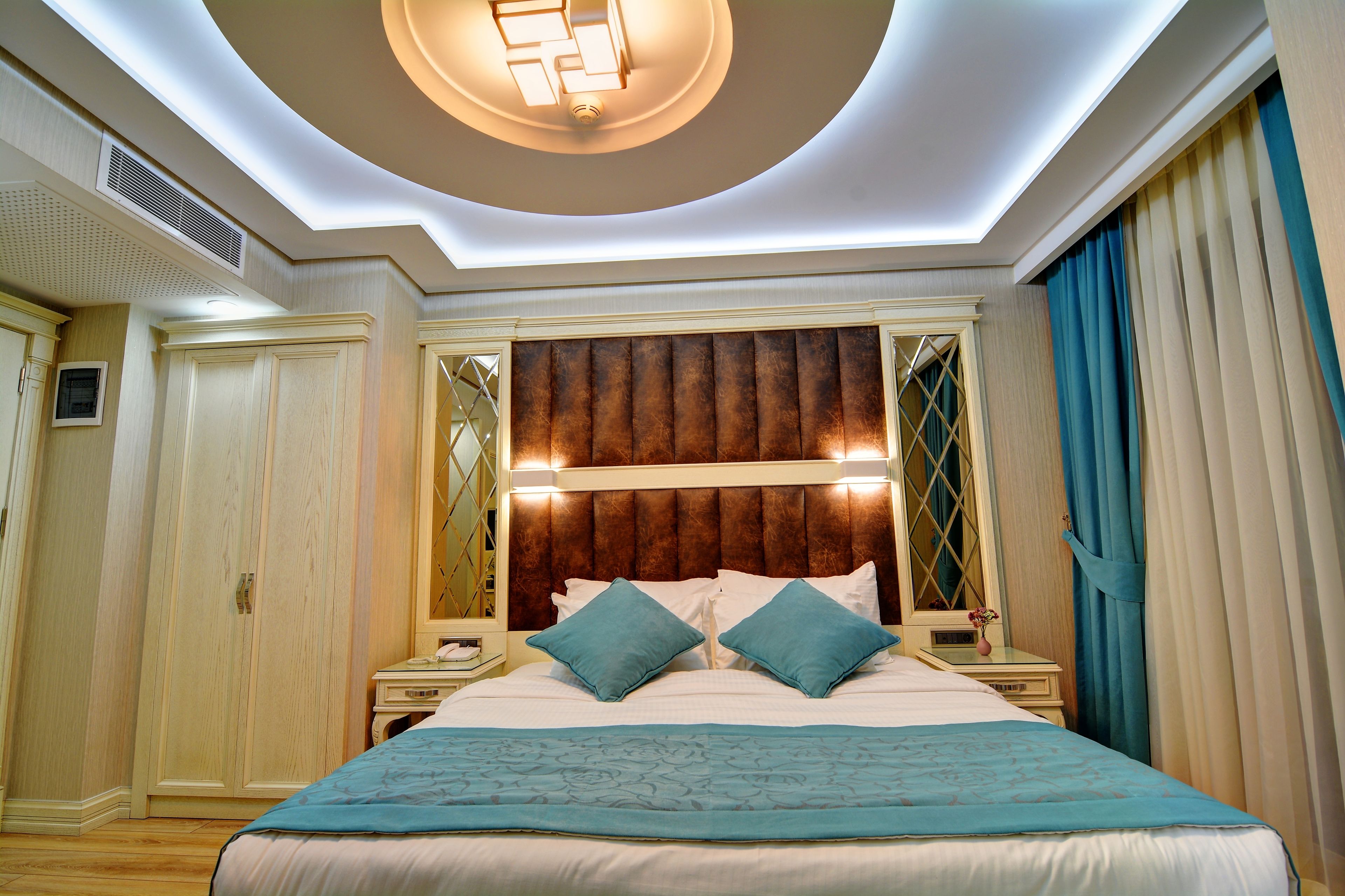 Un dormitorio con una cama grande, cabecera con luces, mesita de noche, espejo y armario.