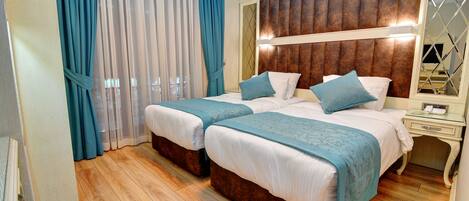 Hotelkamer met twee bedden, een houten hoofdbord, een nachtkastje met telefoon en een groot raam met gordijnen.