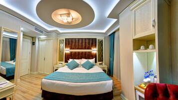 A hotel room with a large bed, a desk, a red chair, and a minibar.