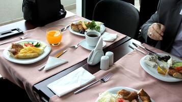 Una mesa servida con platos de comida, un vaso de jugo de naranja y cubiertos.