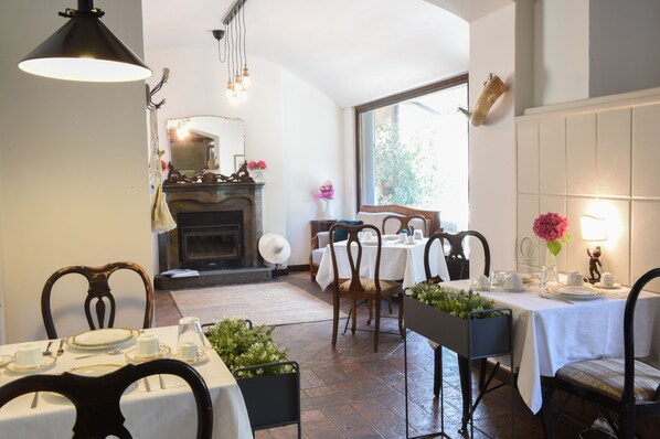 A dining area with tables set for four, a fireplace, and a large window providing natural light. - Il Giardino Segreto (Iseo)
