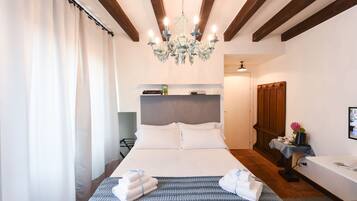 Una habitación de hotel con una cama grande, una araña, una mesita de noche con lámpara y una pequeña mesa con una flor.