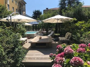 A wooden deck with outdoor furniture, a pool, and umbrellas. - Il Giardino Segreto (Iseo)
