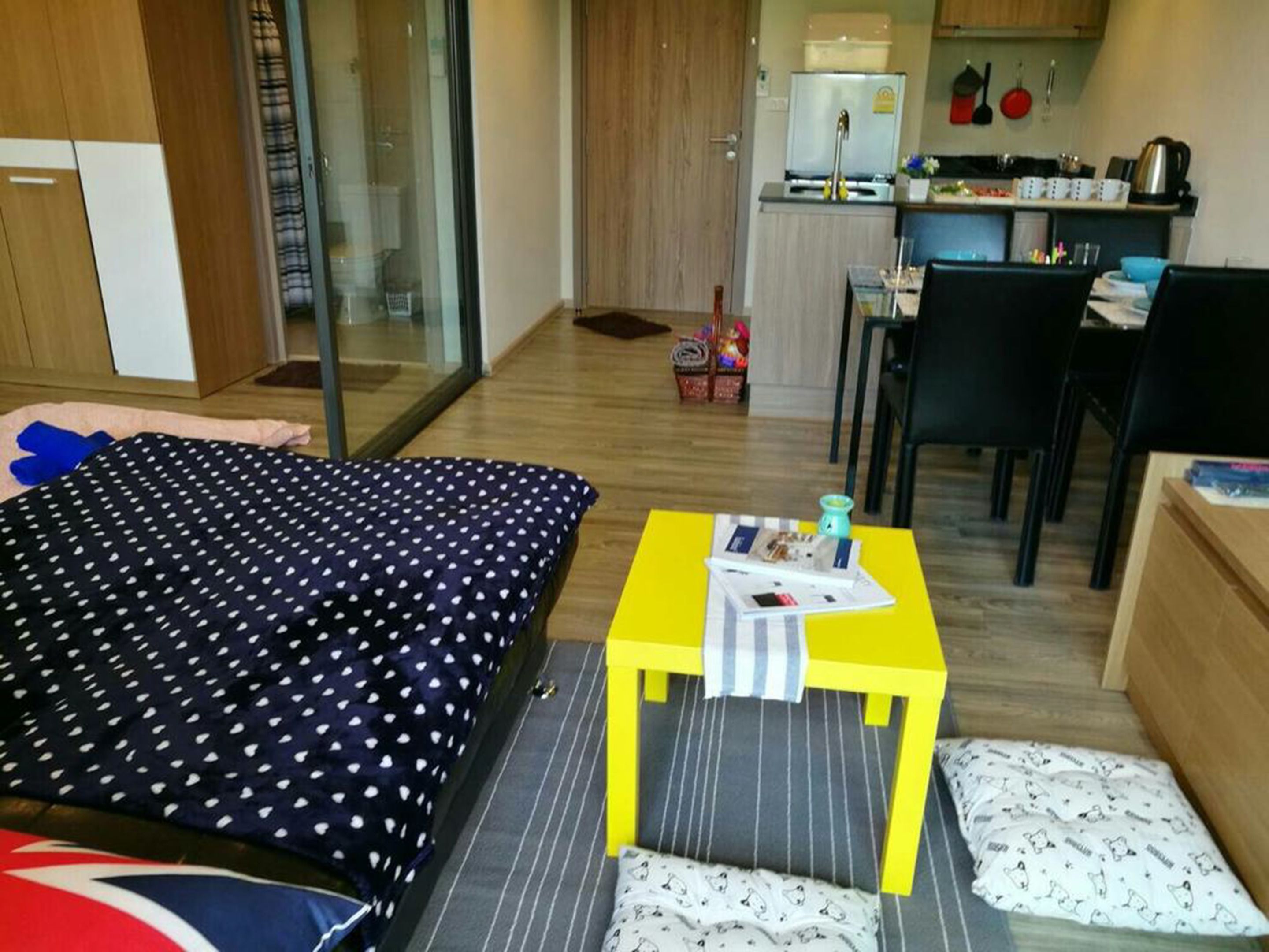 Ein Schlafzimmer mit einem Bett, einem kleinen Tisch mit einer Zeitschrift und einer Küchenzeile im Hintergrund.