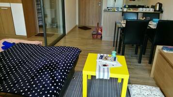 Ein Schlafzimmer mit einem Bett, einem kleinen Tisch mit einer Zeitschrift und einer Küchenzeile im Hintergrund.