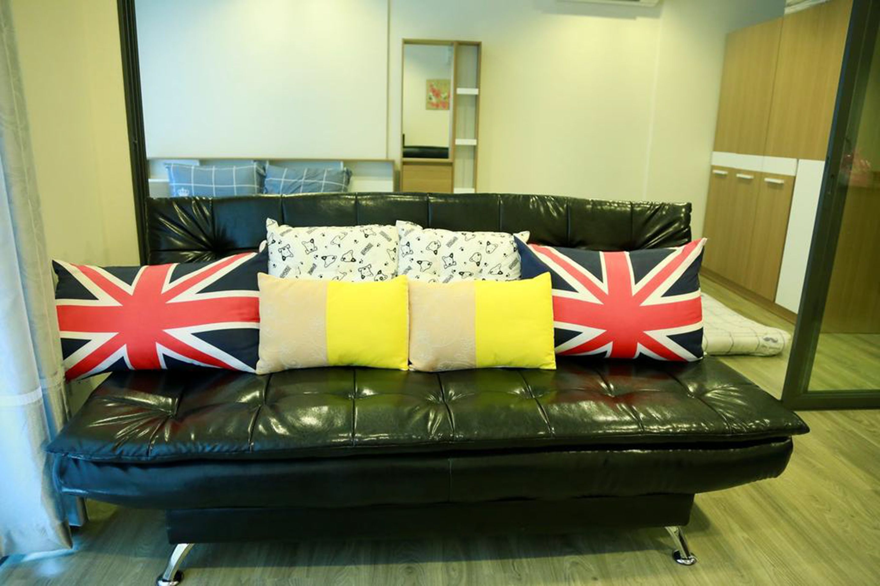 Ein schwarzes Ledersofa mit britischen Flaggen und gemusterten Kissen in einem Raum mit Holzboden und einem Spiegel.