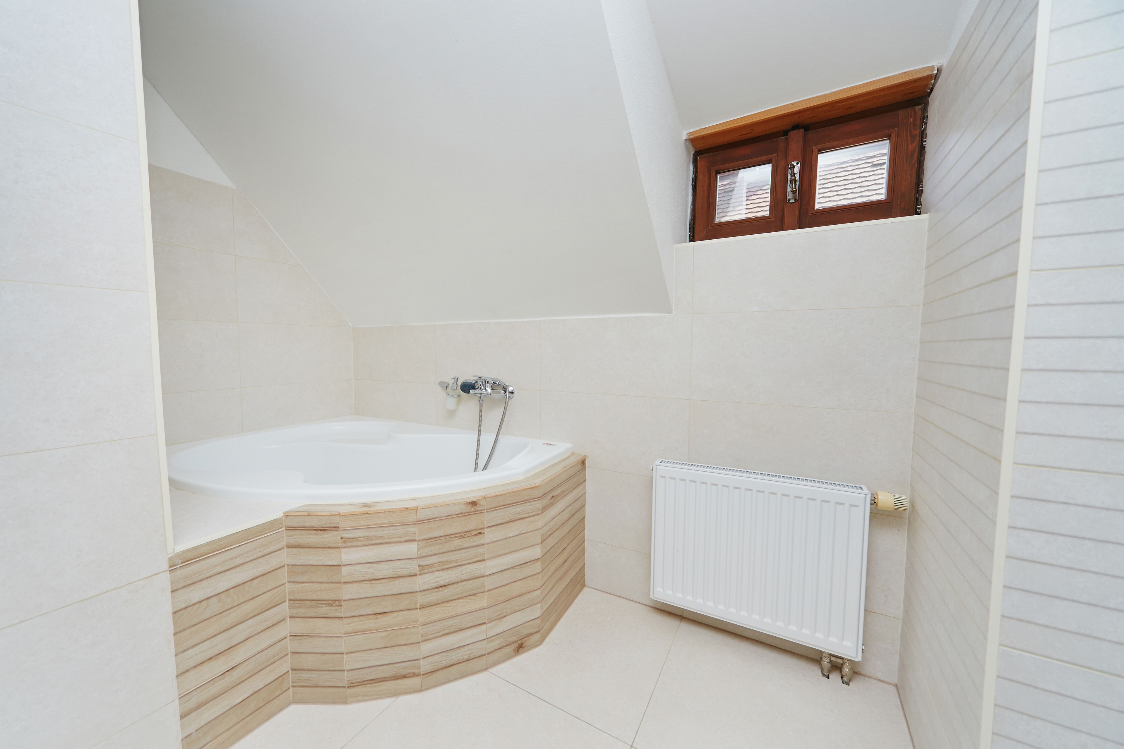 A modern bathroom with a freestanding bathtub, a radiator, and a small window with wooden shutters.