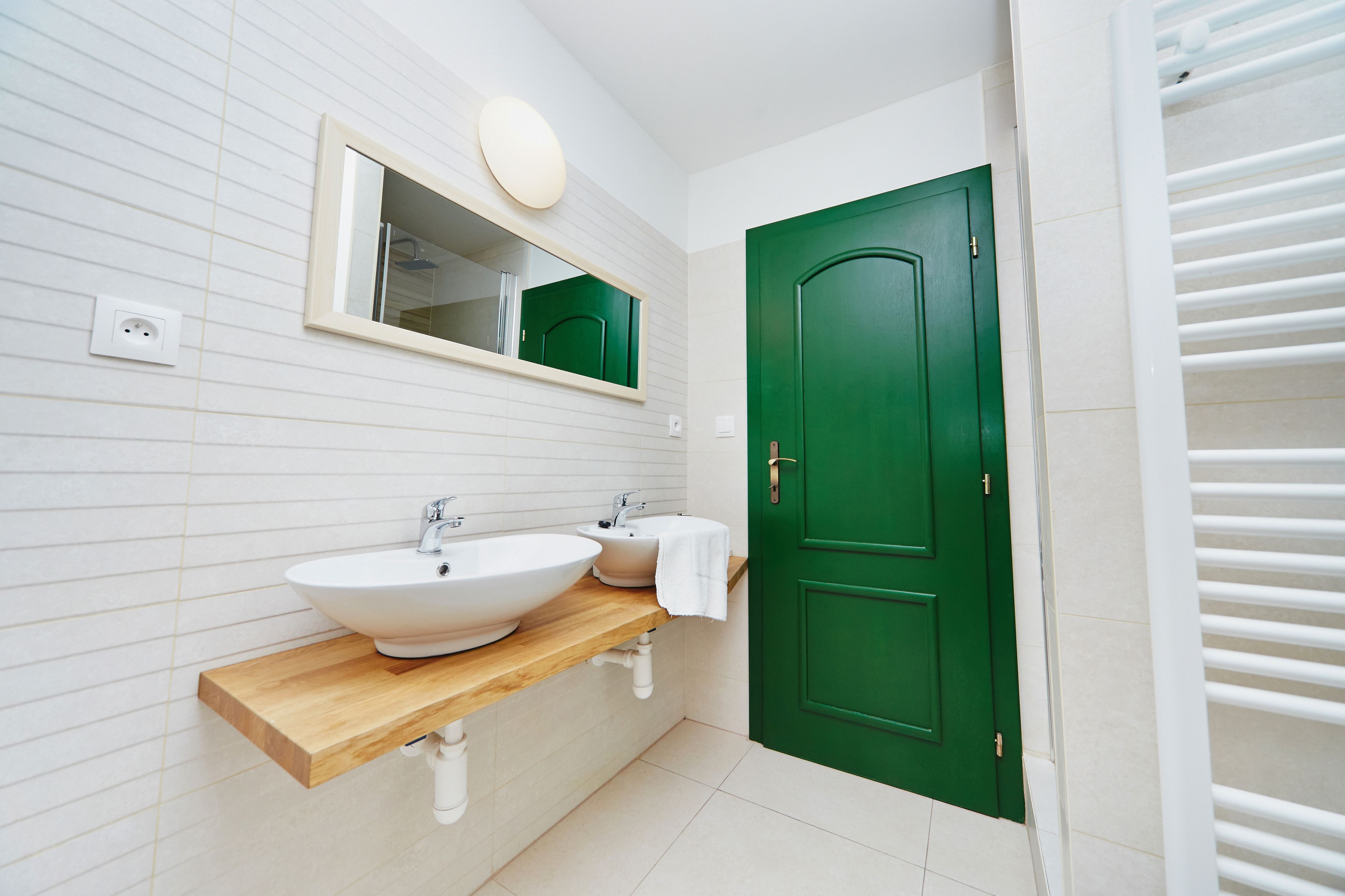 Une salle de bain avec deux lavabos, un miroir et une porte verte.