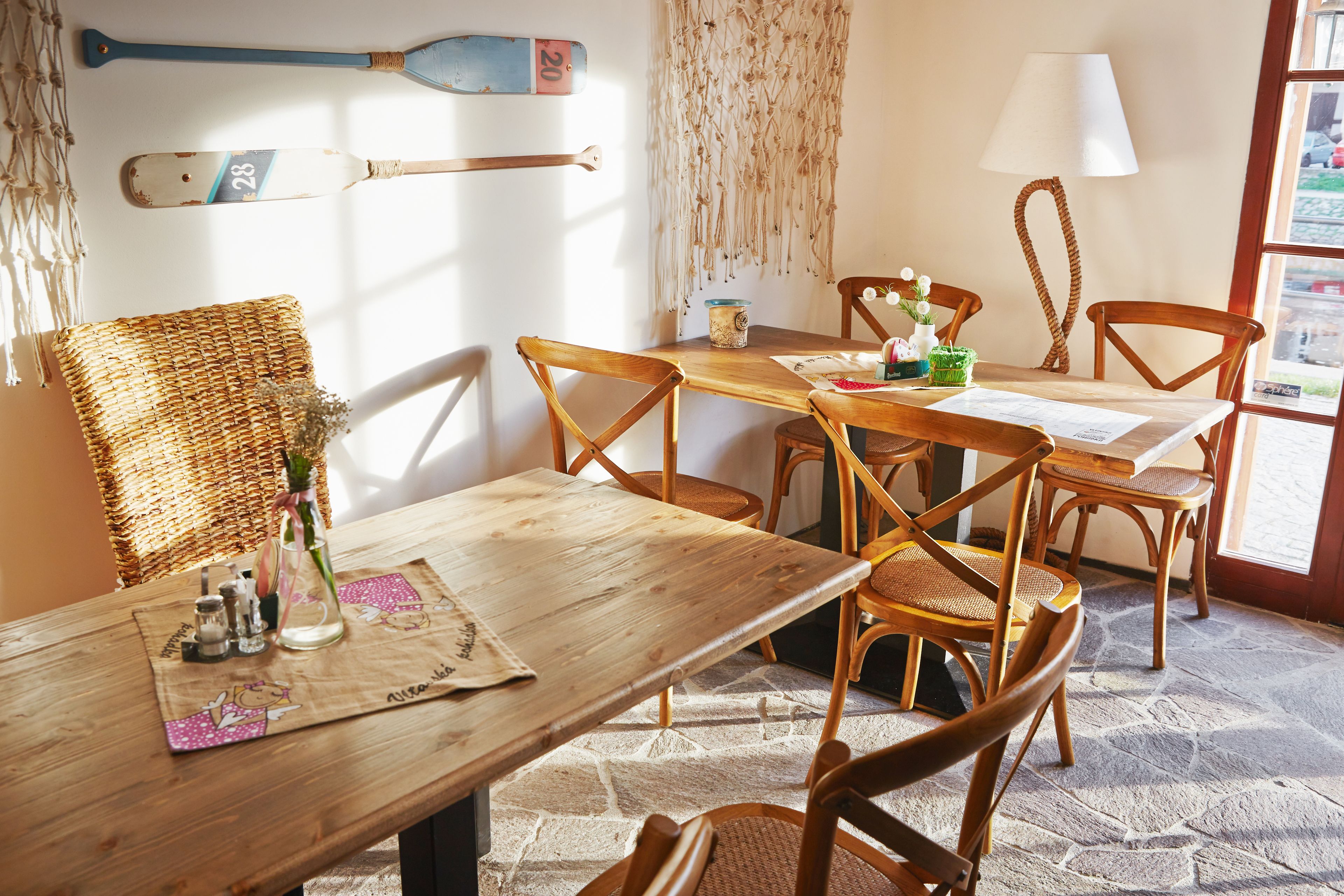 A dining area with wooden tables and chairs, a woven basket, salt and pepper shakers, a vase with flowers, and a wall-mounted paddle.