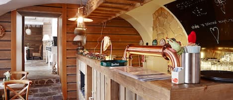 A rustic bar area with wooden beams, a stone wall, and a chalkboard with writing.