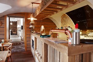 Una zona de bar rústica con vigas de madera, pared de piedra y una pizarra con escritura.