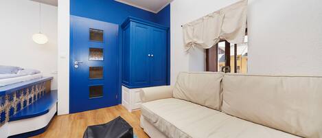 A room with a blue door, a beige sofa, a black bag, and a blue rug.