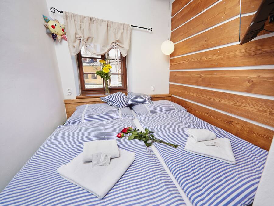 A neatly made bed with striped bedding, a bedside table, a window with curtains, and a wooden wall panel.