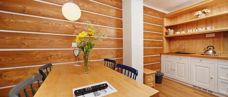 A wooden dining table with chairs, a vase with flowers, and a remote control on a placemat.