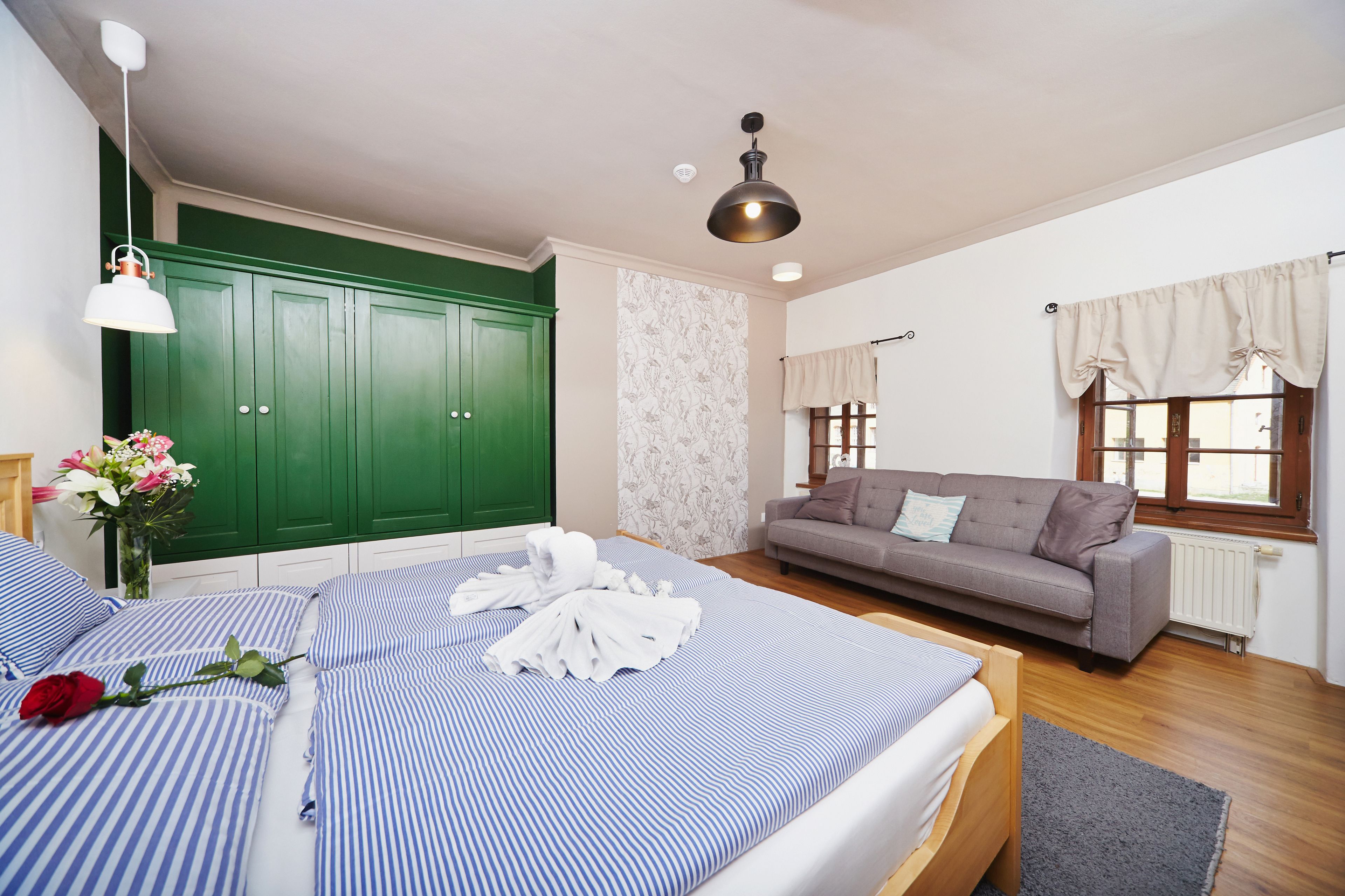 A bedroom with a bed, a green wardrobe, a grey sofa, and a window with curtains.