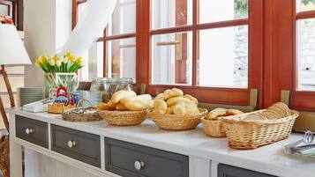 Una encimera de cocina con cestas de pan, un florero con tulipanes amarillos y una ventana con cortinas.
