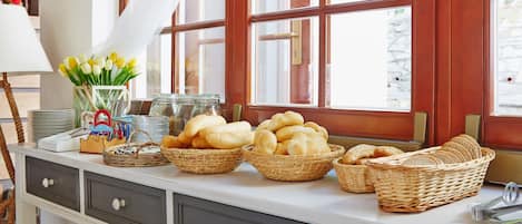 Una encimera de cocina con cestas de pan, un florero con tulipanes amarillos y una ventana con cortinas.