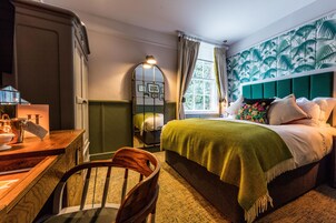 Un dormitorio con cama, escritorio, silla, ventana con cortinas y pared con diseño de hojas.