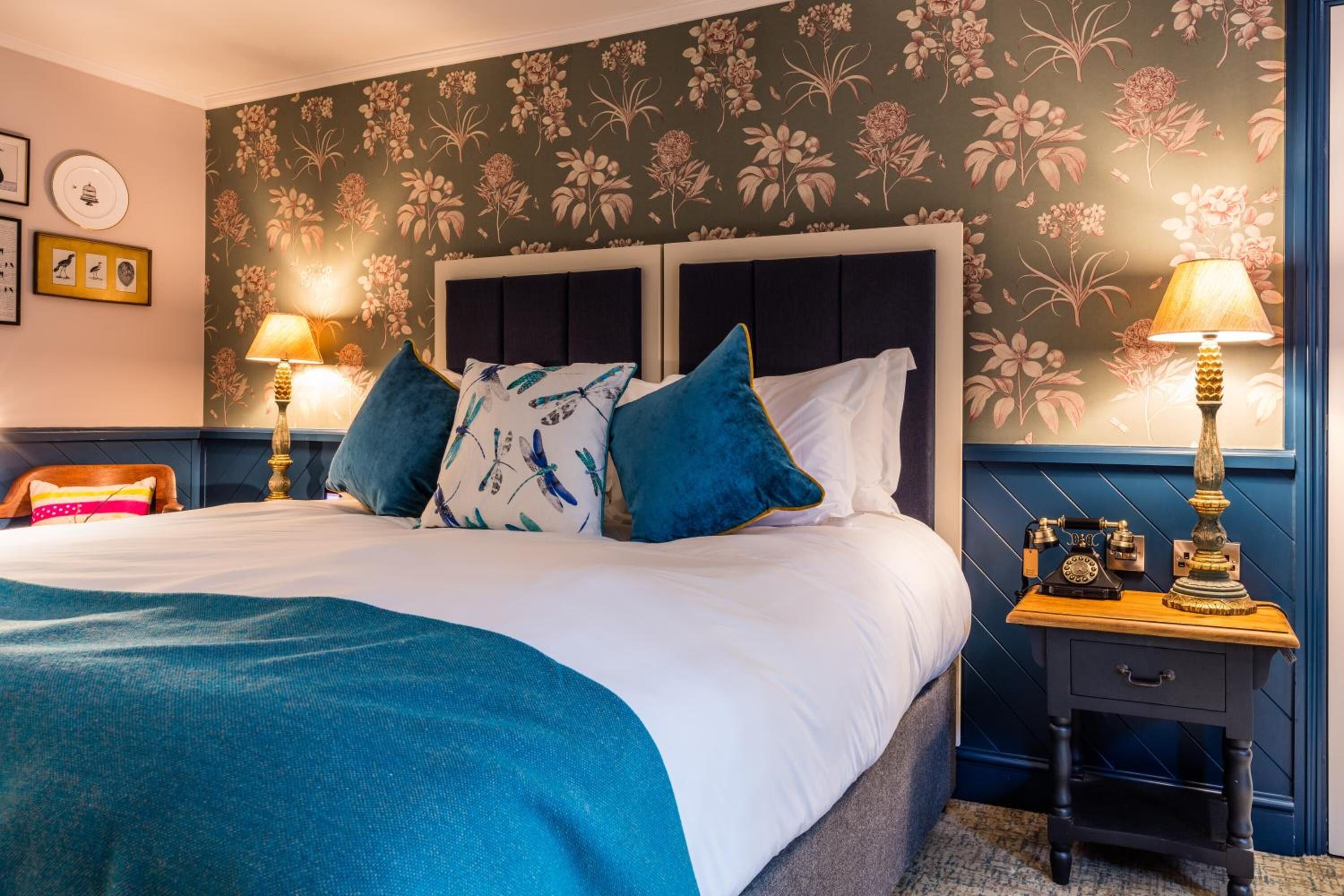 A neatly made bed with a blue blanket, two pillows, and a nightstand with a lamp and a clock.
