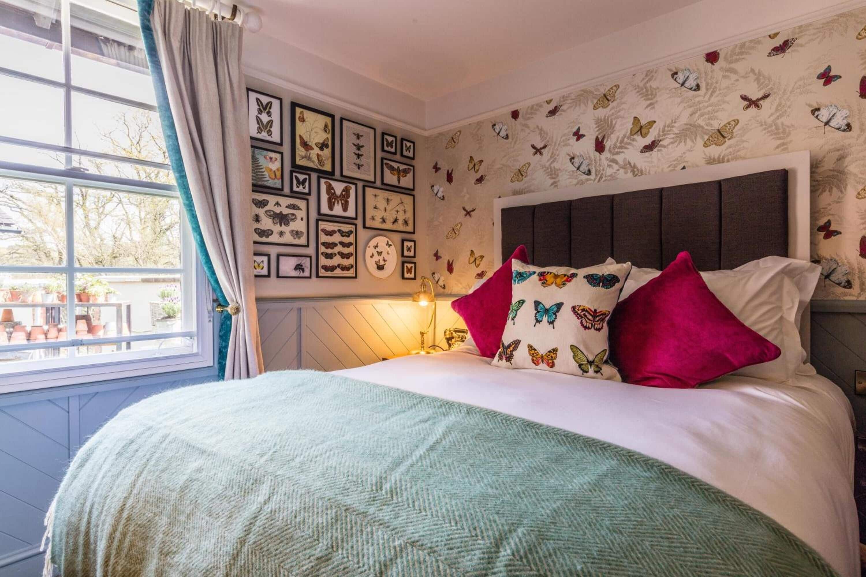 Ein Schlafzimmer mit einem Bett, einem Fenster mit Vorhängen, Wandkunst mit Schmetterlingsmotiv und einem gemusterten Wandteppich.