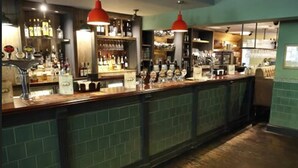 Eine Bar mit einer langen Theke, Regalen voller Flaschen und roten Pendelleuchten.