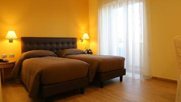 Habitación de hotel con dos camas, suelo de madera y un gran ventanal con cortinas de gasa.