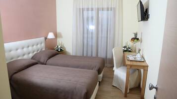 Une chambre d’hôtel avec deux lits, un bureau, une chaise, une télévision et une fenêtre avec des rideaux.