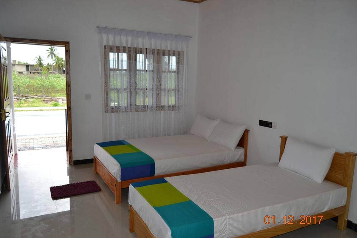 A room with two single beds, a window with sheer curtains, and a door leading outside.