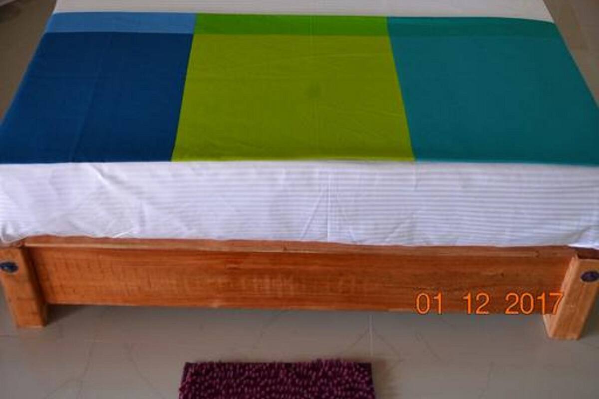 A single-bed room with a wooden frame, white bedding, and a colorful blanket.