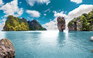 Eine Küstenlandschaft mit klarem türkisblauem Wasser, Felsformationen und sanften, grünen Hügeln unter einem teils bewölkten Himmel.
