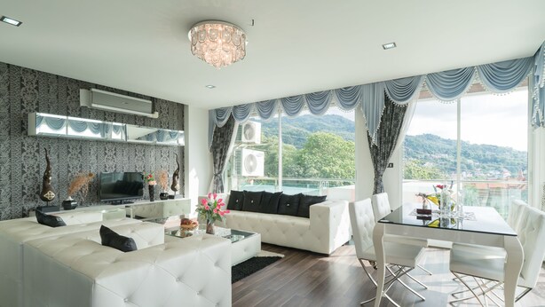 A modern living room with a white sofa, a glass coffee table, and a dining area with a glass table and white chairs.