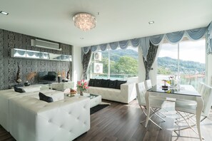A modern living room with a white sofa, a glass coffee table, and a dining area with a glass table and white chairs. - GoldStone Residency Patong , Phuket (Patong)