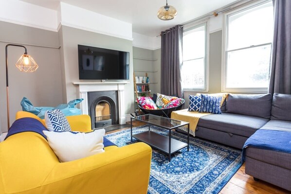 Una sala de estar con chimenea, un sofá, un sillón amarillo y un televisor.