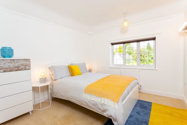 Un dormitorio con cama, lámparas de noche, ventana y cómoda.