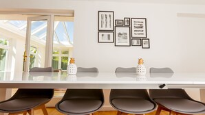 Ein moderner Essbereich mit einem weißen Tisch, vier schwarzen Stühlen und einem Glastisch. An der Wand hängen gerahmte Kunstwerke und auf dem Tisch stehen dekorative Vasen.